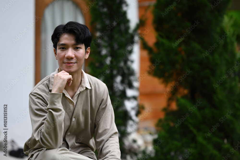 A Portrait of a Young Man sits outdoors, resting his chin on his hand while wearing a soft expression A Portrait of a Young Man sits outdoors, resting his chin on his hand while wearing a soft expression
