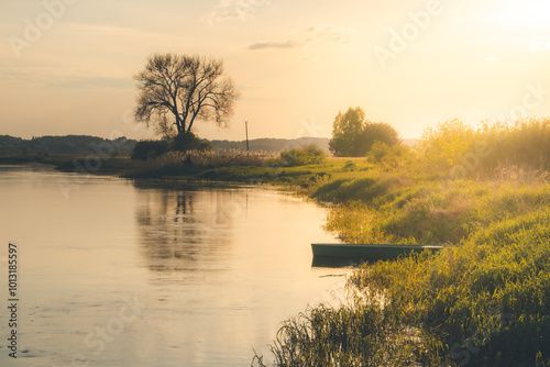 Beautiful landscape of the lake surrounded by the forest. Small lonely fishing boat at the shore. Golden hour. 