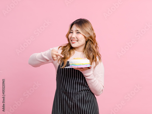 Photo cute happy fun young Asian beautiful female, woman smiling wearing aprons holding cake sweet dessert poses isolated plain pastel light over pink color wall background.