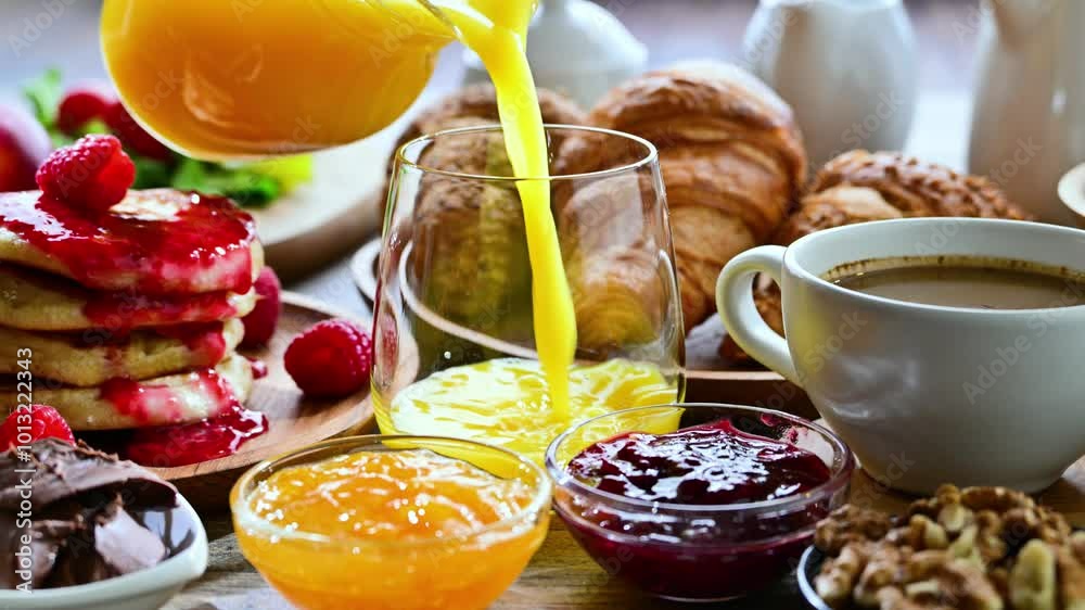 Filling glass with orange juice on table with breakfast