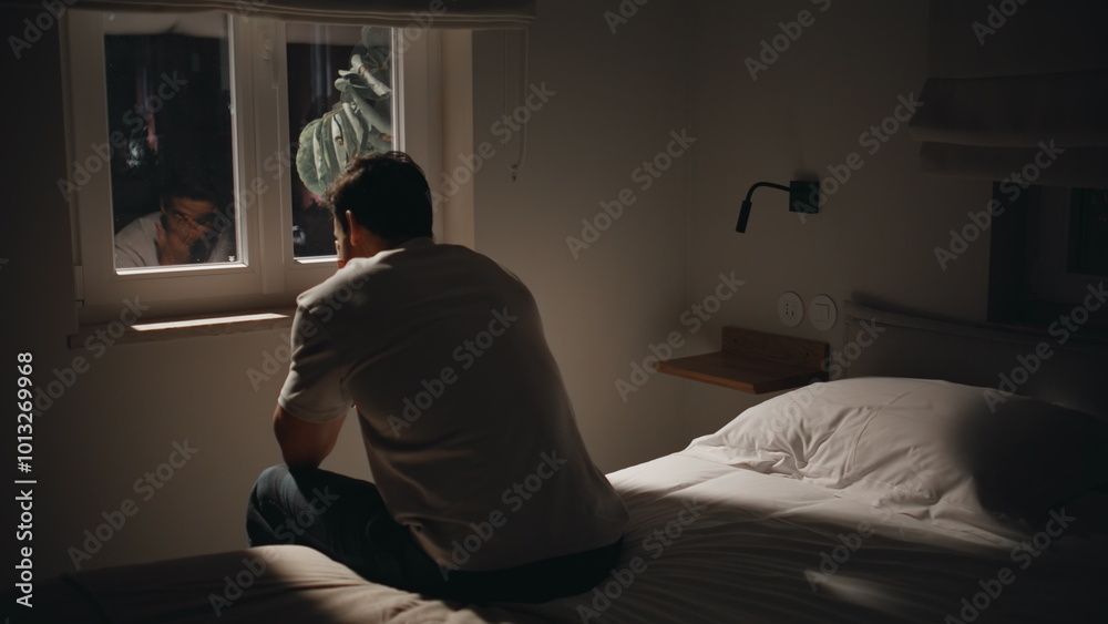 Depressed guy sitting bedding by window at night feeling anxious. Pensive man Depressed guy sitting bedding by window at night feeling anxious. Pensive man