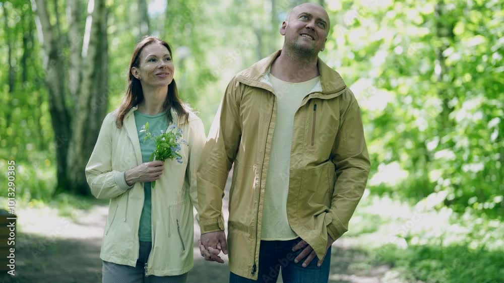 A man and a woman are standing in the forest, exchanging tender glances. He gently holds her head, creating an atmosphere of intimacy among the green nature. A man and a woman are standing in the forest, exchanging tender glances. He gently holds her head, creating an atmosphere of intimacy among the green nature.