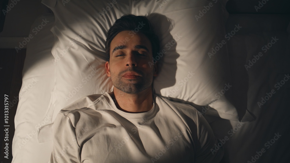 Guy lying dark bedroom at white bedding looking up closeup top view. Man on bed Guy lying dark bedroom at white bedding looking up closeup top view. Man on bed