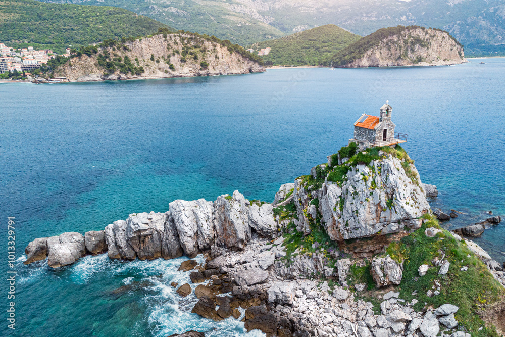 Aerial photography of Petrovac's coastline in Montenegro, highlighting the scenic beauty of its cliffs, islets, and historic Sveta Nedjelja church, a popular destination for travelers.