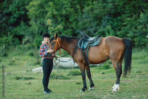 Happy blonde with horse in forest. Woman and a horse walking through the field during the day. Dressed in a plaid shirt and black leggings.