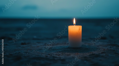 A solitary candle glows warmly on a tranquil beach at dusk, casting a serene ambiance against the cool, darkening sand and distant ocean.