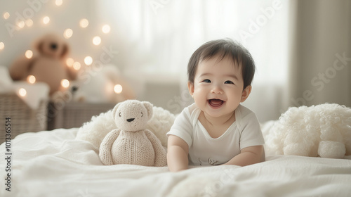 a happy smiling asian baby boy sitting on a bed with a teddy bear and soft pillows.