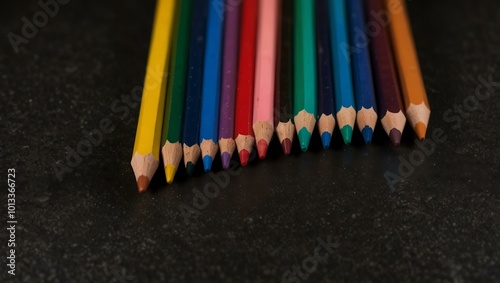 A row of sharpened colored pencils arranged in rainbow order on a black background.