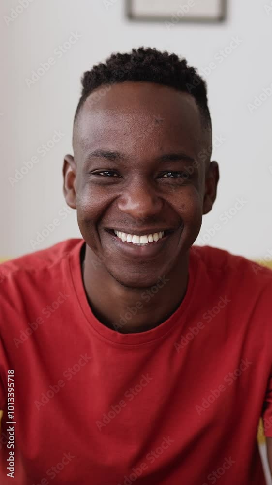 Vertical HD video portrait of happy young black man smiling at camera while sitting on sofa in the living room at home. Vertical HD video portrait of happy young black man smiling at camera while sitting on sofa in the living room at home.
