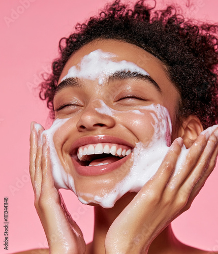 Young smiling black woman washing her face with foam cleanser.