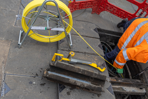 A technician in the field of telephony or communication inserts new cables in a hole in the street to fix some problem