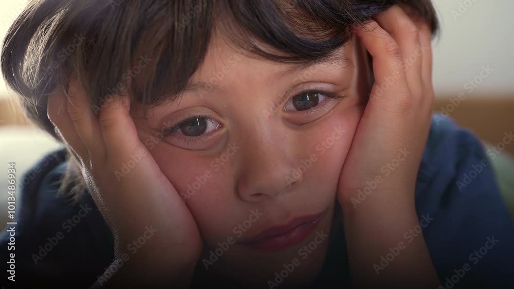 Young boy holding head with both hands, staring intently at a screen, captivated by the content, possibly a movie or cartoon, conveying a sense of focus, curiosity, and childhood wonder