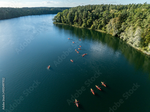 Fototapeta Naklejka Na Ścianę i Meble -  Aerial drone view of people kayaking on a lake surrounded by green forest. Kulka Reserve, Masuria, Poland. Sailing in red kayaks in the Masurian Lake District. Lake Lesk in the Kulka Reserve in Poland