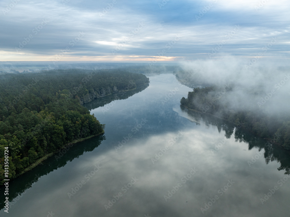 Obraz premium Aerial drone view of a lake surrounded by green forest. Big lake in the fog and clouds. Lake in the Masurian Lake District. Lake Lesk in the Kulka Reserve in Poland. Kulka Reserve, Masuria, Poland.