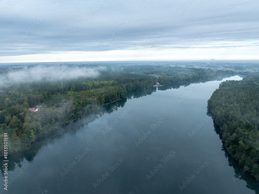 Aerial drone view of a lake surrounded by green forest. Big lake in the fog and clouds. Lake in the Masurian Lake District. Lake Lesk in the Kulka Reserve in Poland. Kulka Reserve, Masuria, Poland. Aerial drone view of a lake surrounded by green forest. Big lake in the fog and clouds. Lake in the Masurian Lake District. Lake Lesk in the Kulka Reserve in Poland. Kulka Reserve, Masuria, Poland.