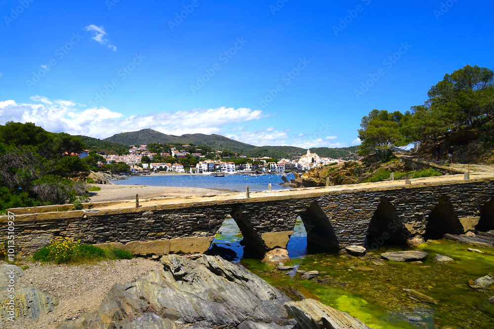 Fototapeta premium old stone bridge Pont des Sortell in the Badia de Cadaqués, white houses of Cadaqués behind, Girona, Figueres, Catalonia, Spain 