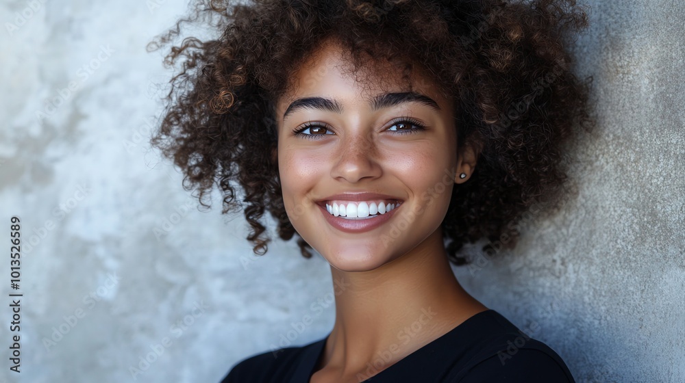A young woman with curly hair and a bright smile looks at the camera. A young woman with curly hair and a bright smile looks at the camera.