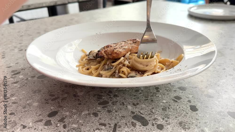 Hand and fork twirl and take out spaghetti creamy chicken alfredo served on a pasta plate on top of grey terrazzo table. Process of eating spaghetti, using fork and lift it up. Table manner. 