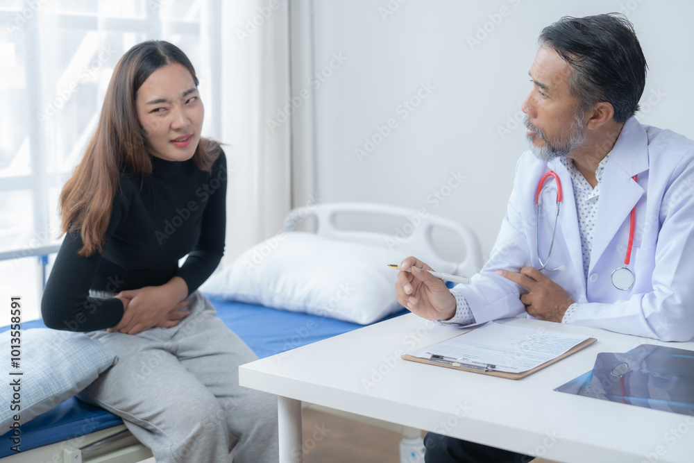 Young woman grimaces in pain while sitting on a hospital bed and describing her symptoms to a doctor, who's listening attentively and taking notes Young woman grimaces in pain while sitting on a hospital bed and describing her symptoms to a doctor, who's listening attentively and taking notes