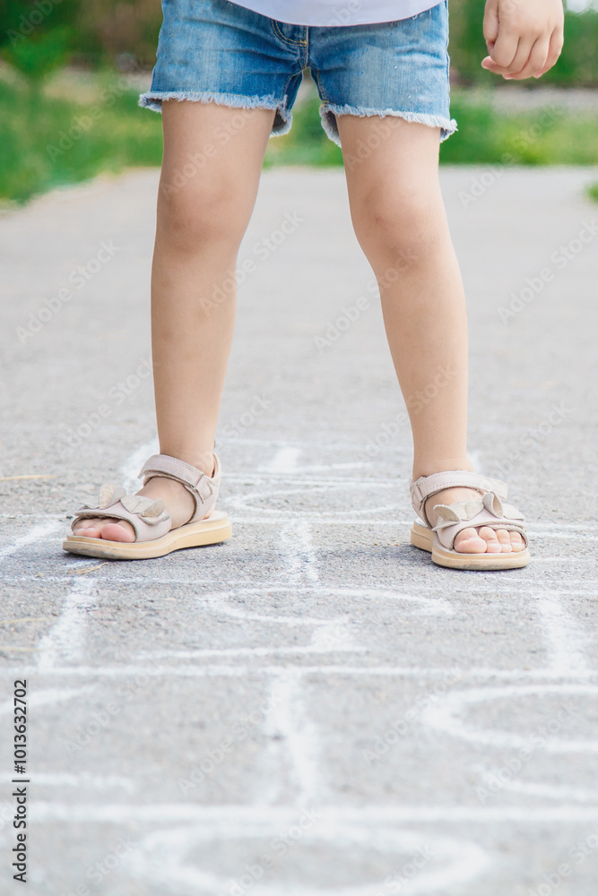 Closeup of little girl legs and hopscotch drawn on asphalt. Child playing hopscotch game on playground outdoors on a sunny day. Summer activities for children. Closeup of little girl legs and hopscotch drawn on asphalt. Child playing hopscotch game on playground outdoors on a sunny day. Summer activities for children.