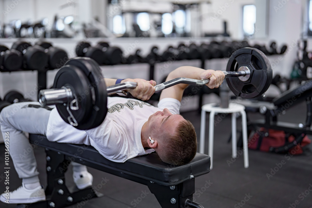 A man in a gym doing a triceps exercise with an EZ-barbell on a bench. A man in a gym doing a triceps exercise with an EZ-barbell on a bench.