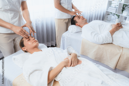 Caucasian couple enjoying relaxing anti-stress head massage and pampering facial beauty skin recreation leisure in dayspa modern light ambient at luxury resort or hotel spa salon. Quiescent