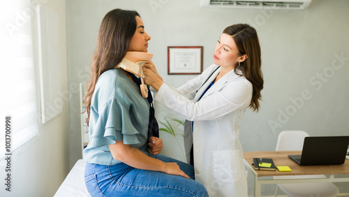 Attractive woman doctor is fitting a cervical collar on a female patient seated on an examination table photo