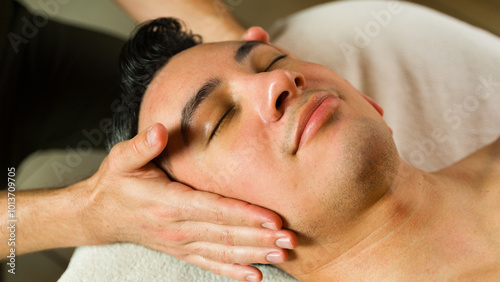 Closeup of a man lying on a massage table, enjoying a therapist's soothing head massage for wellness and relaxation