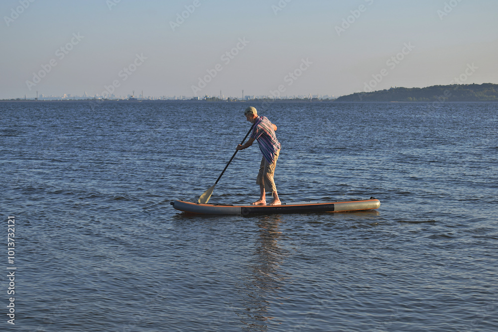 Naklejka premium An elderly man pours on SUP while standing.