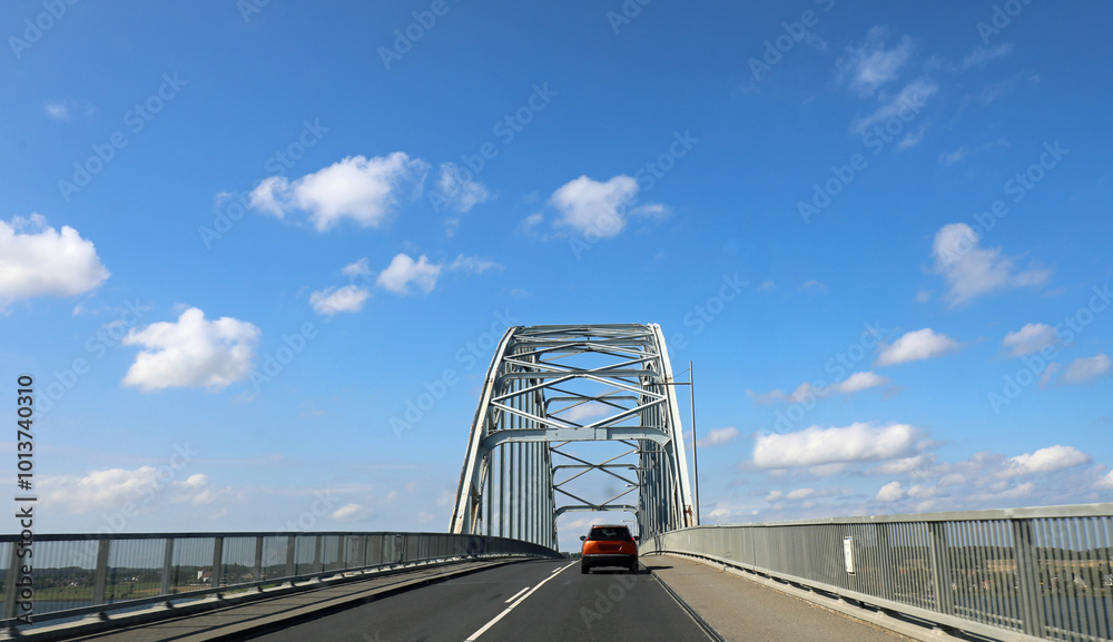 Fototapeta premium road with a large metal truss bridge and a car crossing it
