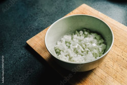 Obraz na płótnie Finely diced onion in a beige bowl on a wooden used cutting board. Dark kitchen countertop w salonie