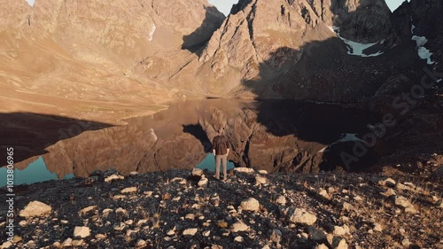 Aerial zoom out view young male photographer working outdoors in mountain environment taking landscape picture of highland alpine Toabavarchkhili lake on beautiful sunset on best golden hour light. photo