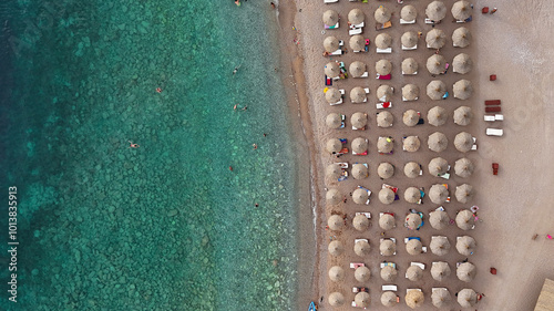 The photo above shows rows of monochromatic beach umbrellas lined along the coast. The sea near the shore looks crystal clear and transparent, turquoise in color. Horizontal photo for a magazine.