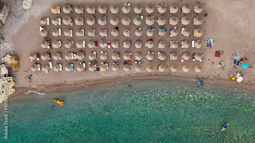 The photo above shows rows of monochromatic beach umbrellas lined along the coast. The sea near the shore looks crystal clear and transparent, turquoise in color. Horizontal photo for a magazin