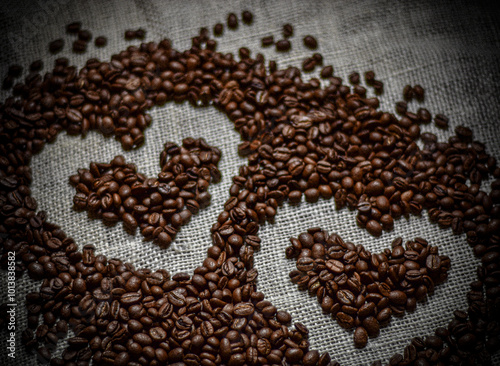 The image shows a close-up of dark, roasted coffee beans. One bean is in focus, highlighting its natural seam. The rest are blurred, creating a rich, textured background.

