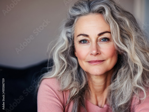 A woman with wavy gray hair smiles warmly in a cozy indoor setting during daylight hours