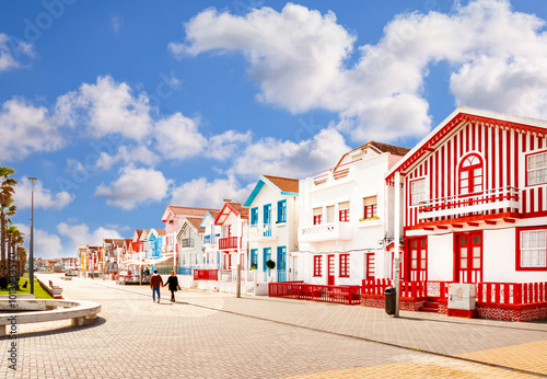 A couple walking hand in hand on Costa Nova beach in Aveiro. Colorful houses with typical stripes on this beach in Aveiro in Portugal.