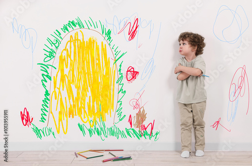 Upset little child near white wall with drawings