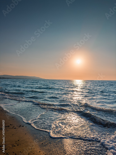 Sunset Over Calm Beach With Gentle Waves Lapping at the Shore and Distant Hills on the Horizon