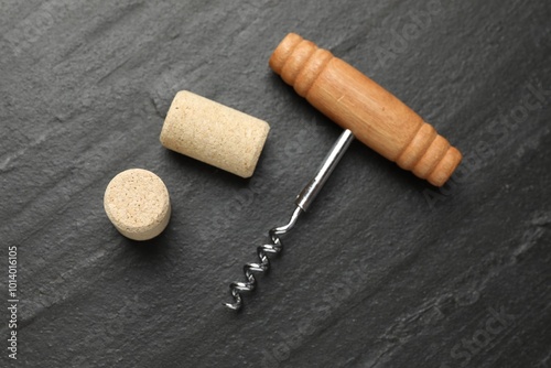 Corkscrew with wooden handle and corks on black table, top view photo