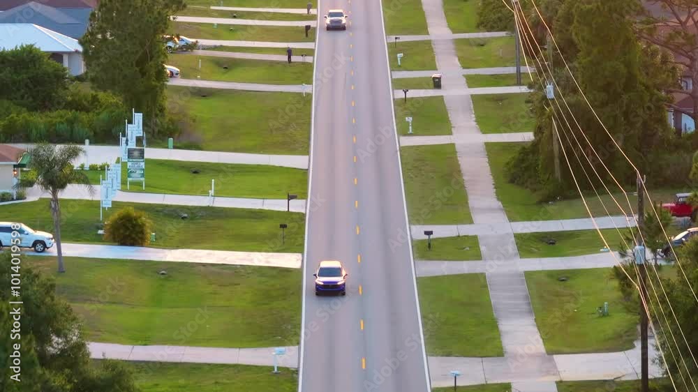 Cars driving on suburban street in Florida small town. American rural landscape with private houses in North Port quiet residential area. Cars driving on suburban street in Florida small town. American rural landscape with private houses in North Port quiet residential area.