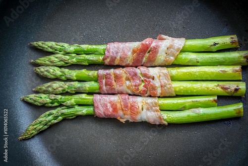 Gourmet asparagus with wrapped bacon meal in black pan. Delicious savory menu from star cuisine. Fresh seasonal cooked ingredients with tender bite. Recipe for oil grilled vegetable food photo