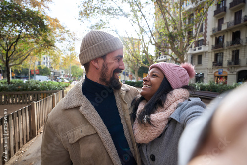Tablou pe pânză Winter portrait of happy young tourist couple taking selfie looking at each other outdoors in a city