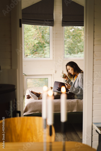 A woman relaxes in a bright, serene room, sipping coffee while focused on her book. The natural light from the windows enhances the cozy atmosphere.