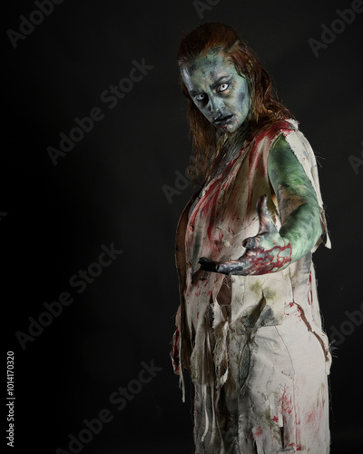 Close up portrait of scary female model wearing spooky halloween costume wearing, ripped clothes and fake blood like an undead apocalyptic zombie character. Isolated figure on dark studio background