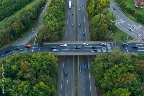 An aerial view of a highway with cars driving on it. The highway is surrounded by trees and fields.