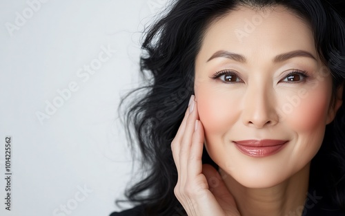 A serene woman with flowing black hair gently smiles, showcasing her natural beauty and radiance against a soft background.