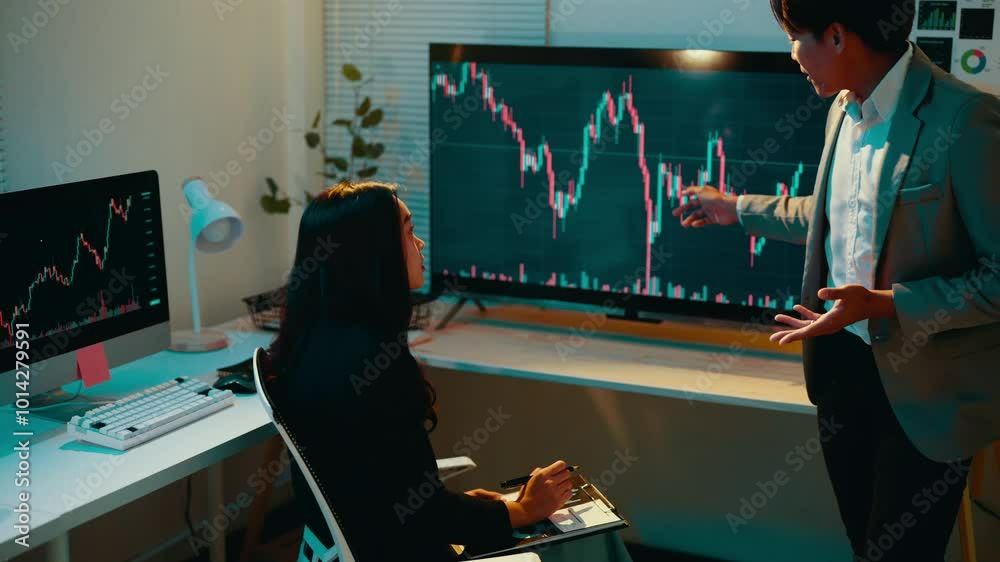 Male financial advisor gestures while explaining stock market fluctuations to a female client in a formal office setting at night, fostering an engaging discussion about investment strategies