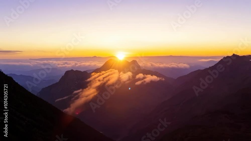 A glowing sunrise lights up the mountain peaks and clouds in a breathtaking view. The serene sky meets the rugged mountains casting shadows over the landscape.