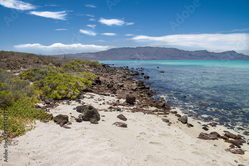 Beach with crystal clear water and white sands with rocky parts on Coronado Island Baja California Sur Mexico. Blue sky and mountains in the background summer vacations morning